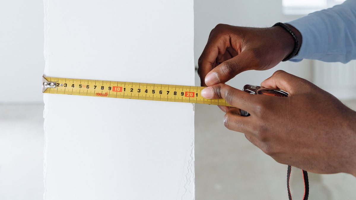 Hands holding a tape measure against a white wall during renovation planning.