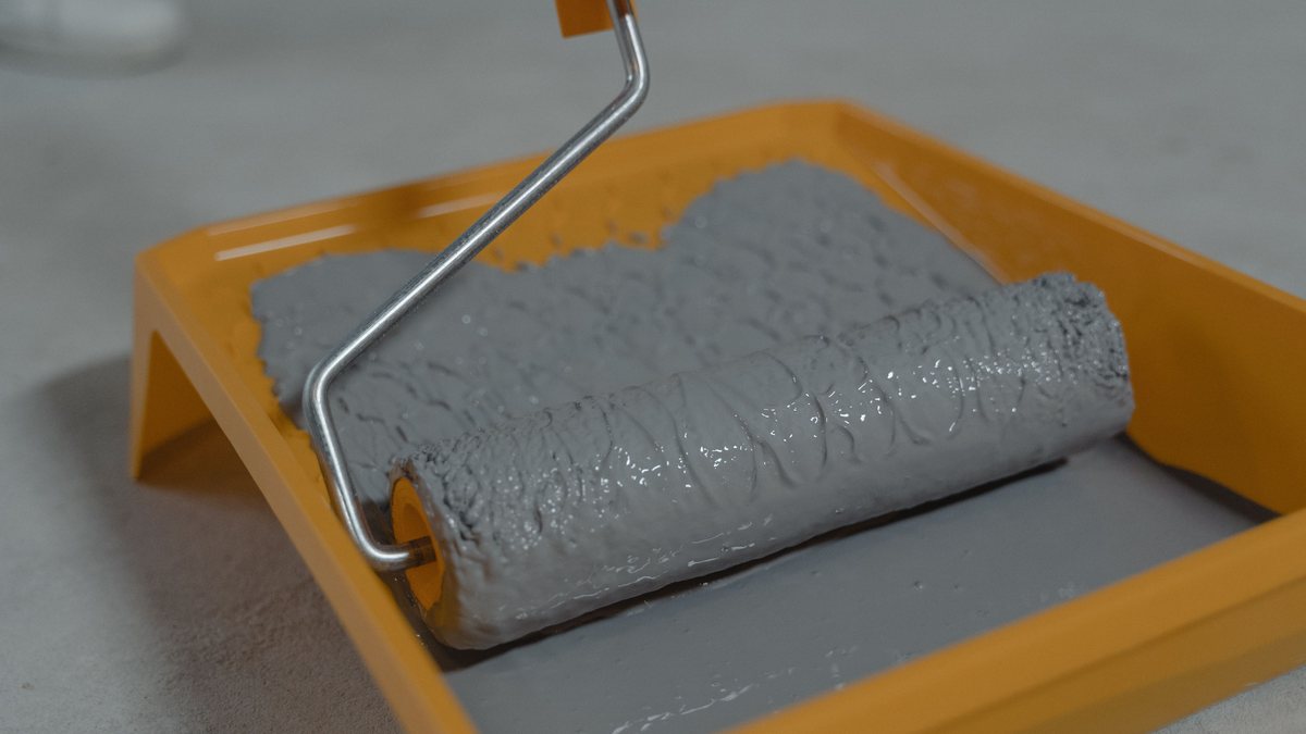 Gray paint-coated roller resting in an orange tray before a coverage test.